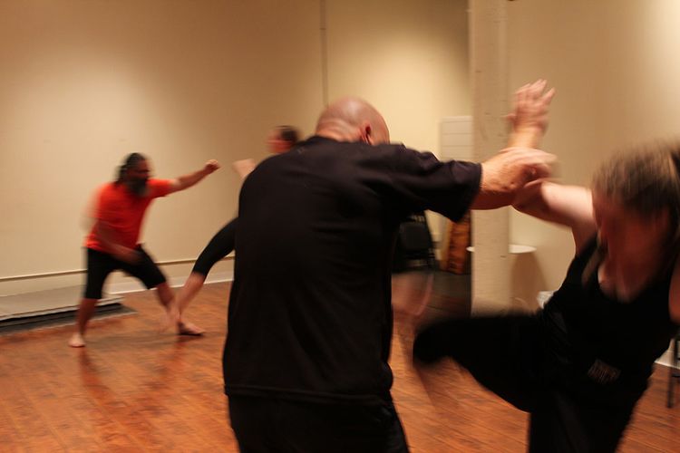 Four people sparring on a hardwood floor, blurred in motion